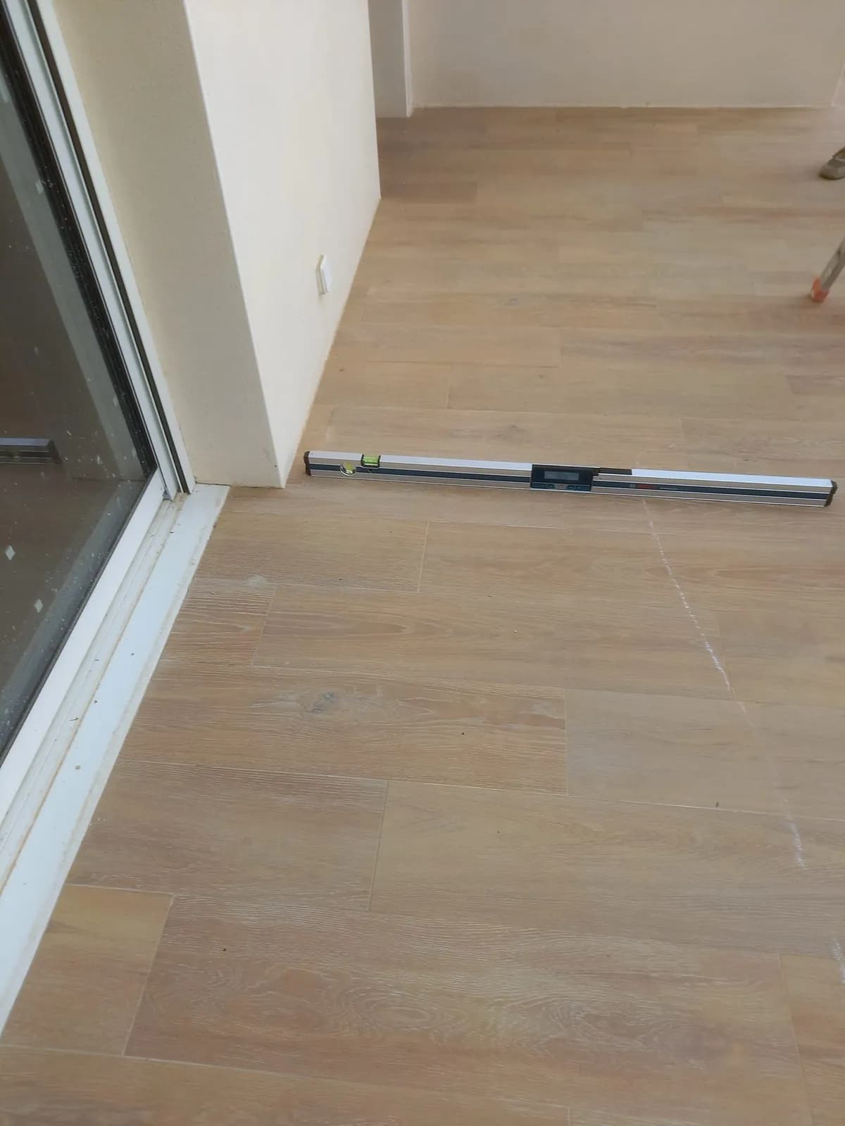Règle niveau posée au sol devant une baie vitrée pour contrôler la pente du revêtement